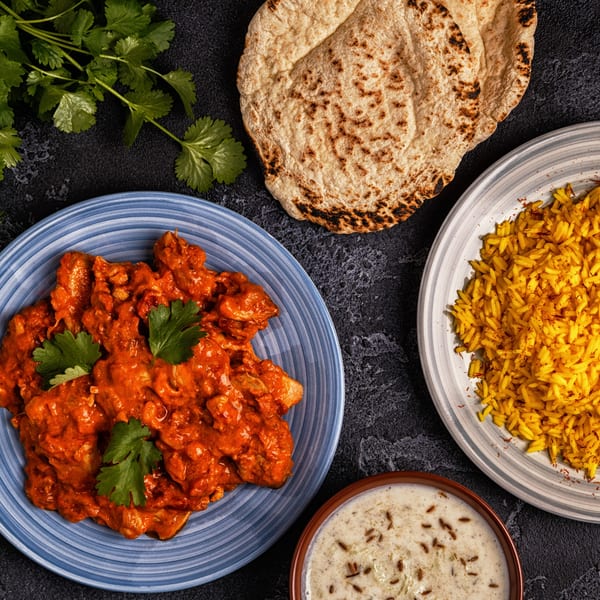 Tikka House Indian Eatery's butter chicken, saffron rice, naan bread, and raita, garnished with cilantro.