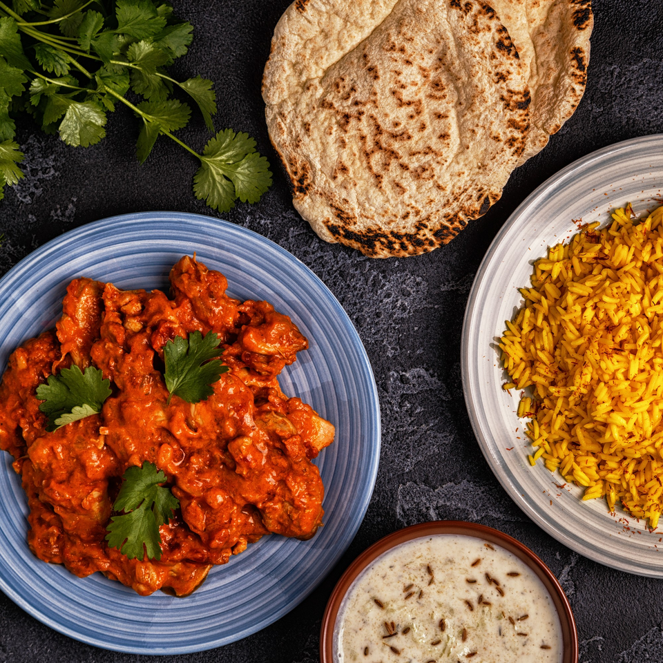Tikka House Indian Eatery's butter chicken, saffron rice, naan bread, and raita, garnished with cilantro.