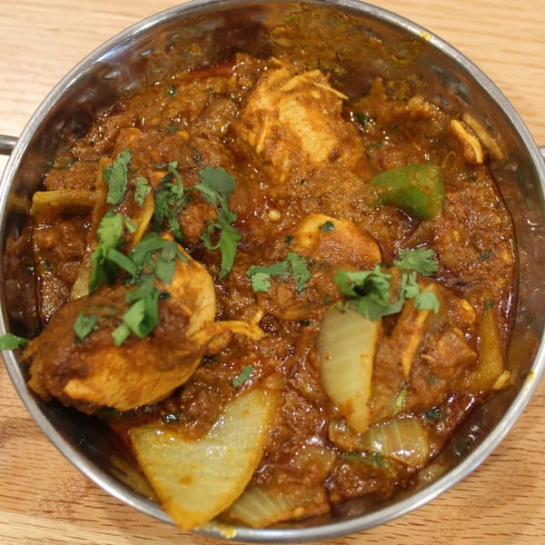Tikka House Indian Eatery's chicken curry with onions, green peppers, and cilantro in a metal bowl.