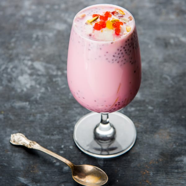 A tall glass of pink Falooda, an Indian dessert drink, with colorful toppings and a spoon.