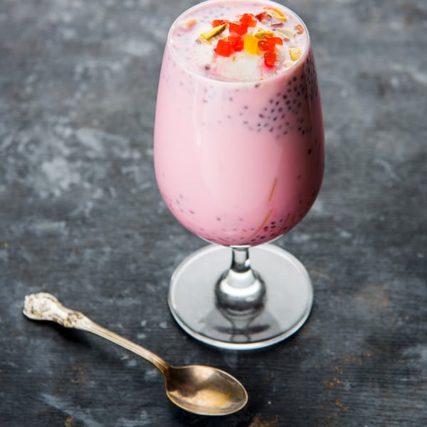 A tall glass of pink Falooda, an Indian dessert drink, with colorful toppings and a spoon.