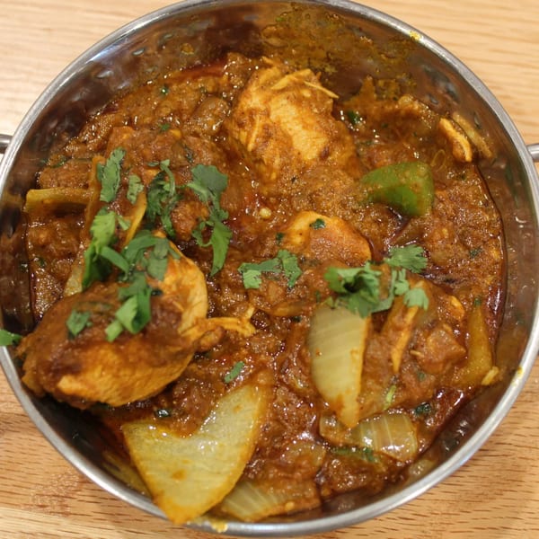 A close-up of Tikka House's chicken curry with onions, green peppers, and cilantro in a metal bowl.