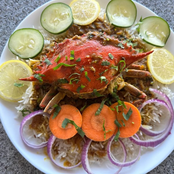 Tikka House Indian Eatery's crab curry with rice, garnished with lemon, cucumber, carrots, and red onion.