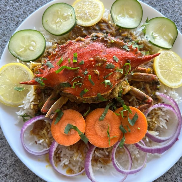 Tikka House Indian Eatery's crab curry with rice, garnished with lemon, cucumber, carrots, and red onion.