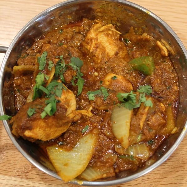 Tikka House Indian Eatery's chicken curry with onions, green peppers, and cilantro in a metal bowl.