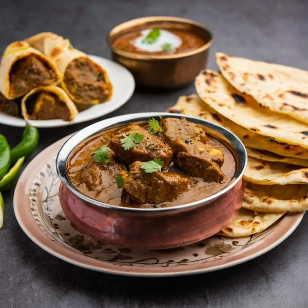 Tikka House Indian Eatery's chicken curry, naan, dal makhani, and kathi rolls on a dark surface.