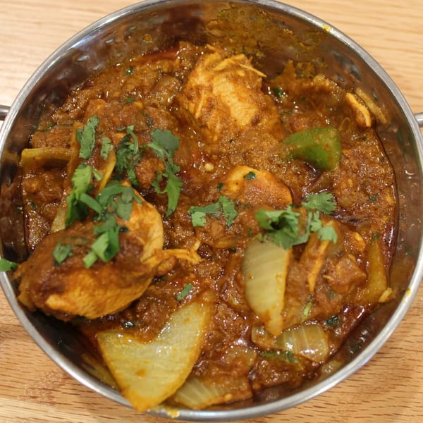 Tikka House Indian Eatery's chicken curry with onions, green peppers, and cilantro in a metal bowl.