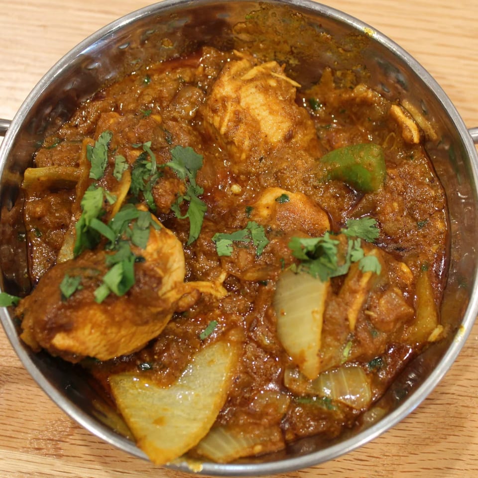 Tikka House Indian Eatery's chicken curry with onions, green peppers, and cilantro in a metal bowl.