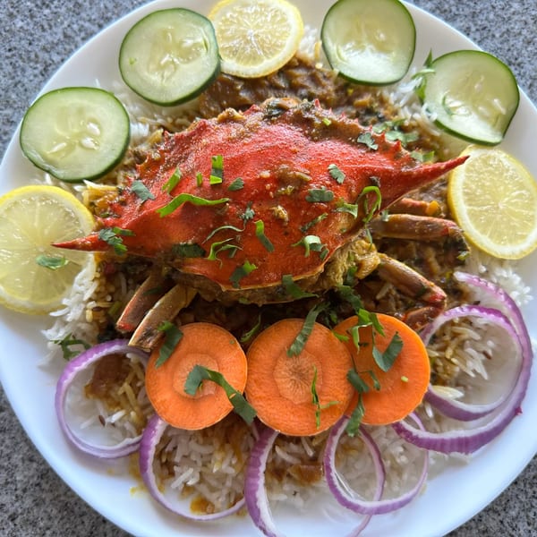 Tikka House Indian Eatery's crab curry with rice, garnished with lemon, cucumber, carrots, and red onion.
